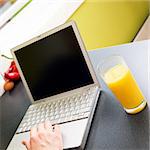 A person used a laptop computer while drinking a glass of orange juice