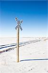 Railroad crossing sign by tracks in rural desolate snowy landscape.