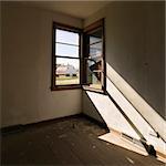 Dark empty abandoned room with sunrays stretching across wall from corner window.