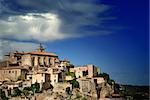 View of ancient medieval hilltop town of Gordes in France, under a dramatic, partly cloudy sky.