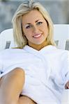 A beautiful young blond woman in a white bath robe sitting on a sunlounger and lit with diffused natural light