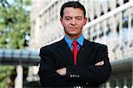 Good looking caucasian / white business man standing with arms folded against an office building.