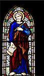 detail of victorian stained glass church window in Fringford depicting St Luke the Evangelist, a scroll in his hands with the beginning of his gospel in latin "Fuit in diebus herodes"