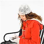 Caucasian young adult female in winter clothing sitting using PDA.