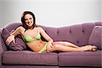 Young Caucasian woman reclining on couch in lingerie smiling at viewer.