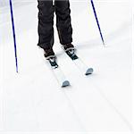 Close up of skier legs boots poles and skis standing on slope.