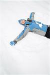 Attractive smiling mid adult Caucasian woman wearing blue ski clothing lying in snow with eyes closed making snow angel.