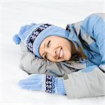 Attractive smiling mid adult Caucasian woman wearing blue ski clothing lying in snow looking at viewer.