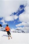 Skier in bright colored outfit skiing down a ski slope in the mountains during winter with blue cloudy skies in the background.