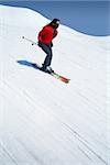 Skier in bright colored outfit skiing down very fast a ski slope in the mountains during winter with blue cloudy skies in the background.