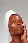 African-American girl applying facial skincare product (gray background)
