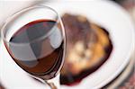 Red wine in a glass with shallow depth of field and soft focus, in front of a meal with a rich, red wine sauce.
