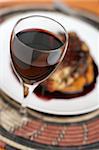 Red wine in glass with shallow depth of field in front of a meal with a rich red wine sauce.