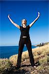 Caucasian mid-adult woman standing on Maui, Hawaii coast with arms outstretched and eyes closed.