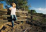 Western woman leans against a decrepit old split rail fence.