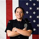 Portrait of mid adult Caucasian policewoman standing with arms crossed with American flag as backdrop smiling at viewer.