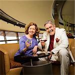 Mature Caucasian couple sitting in bar lounge having drinks and smiling.