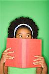 African American girl with book held up to face looking suspiciously to the side.
