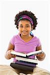 African American girl with large stack of books smiling at viewer.