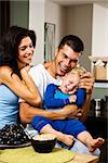 Caucasian family with toddler son in kitchen at breakfast smiling and tickling.