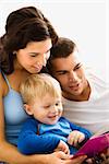 Caucasian parents and toddler son reading book together.