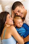 Caucasian mid adult parents cuddling with toddler son sleeping in bed.