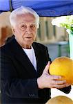 Old man at the marketplace picking a melon
