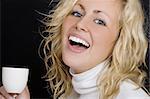 Studio shot on a black background beautiful young blond woman wearing white, laughing and drinking coffee.