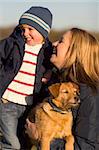 A mother her young son and the family dog together laughing on a park bench.