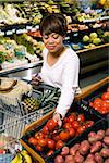 Middle aged African American woman selecting tomatoes from grocery store produce.