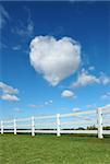 Heart cloud in the sky with white fence in the foreground.
