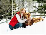 Woman hugging dog and smiling in snow covered Colorado landscape.