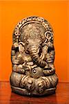 Statue of Hindu elephant Ganesha against orange wall.