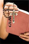 Woman holding Holy Bible open with rosary and crucifix in hand.