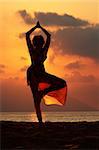 Woman doing yoga exercise on the beach at sunset