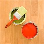 High angle of paintbrush with paint cans on wood floor.