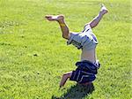Little boy standing on his head on a grass