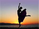 Dramatic image of a woman dancing by the ocean at sunset