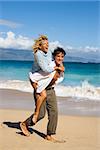 Woman riding piggyback on man while both smile and laugh on Maui, Hawaii beach.