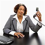 Businesswoman sitting at desk holding telephone receiver out away from head looking with strange expression.