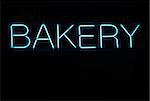 Illuminated blue bakery neon sign on a black background