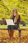 20-25 years old beautiful sexy woman portrait working on laptop computer in natural autumn outdoors on park bench