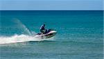A jetskier speeds fast along the ocean surf on a beautiful blue day