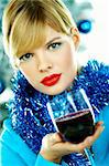 Beautiful young woman holding glass of red wine next to christmas tree on white background