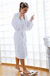 young blond woman wearing a white bathrobe doing weight control in her bathroom
