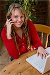 A beautiful young woman working on her laptop at home and talking on a mobile phone