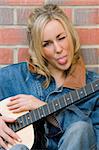 A beautiful young woman leaning on her guitar, winking and sticking out her tongue