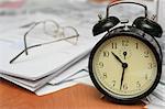 Black alarm clock on a table where other documents lay