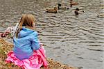 small child sitting at lake shore and feeding ducks