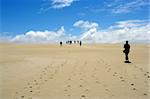 Group of people walking on sand dunes.